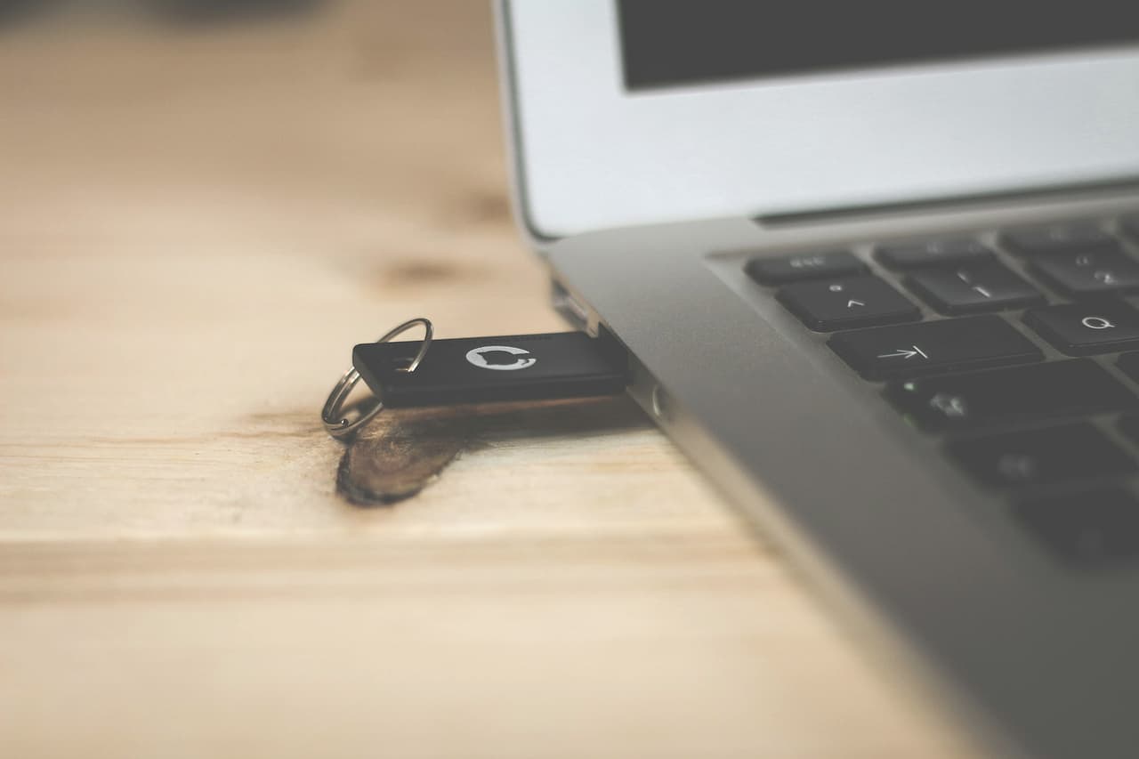 A USB drive plugged into the side of a laptop on a wooden desk