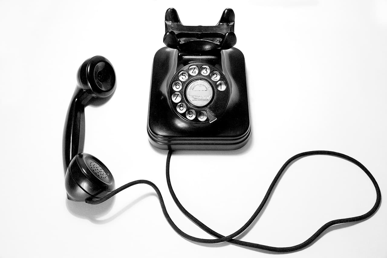 A black rotary telephone with its handset lifted off the cradle