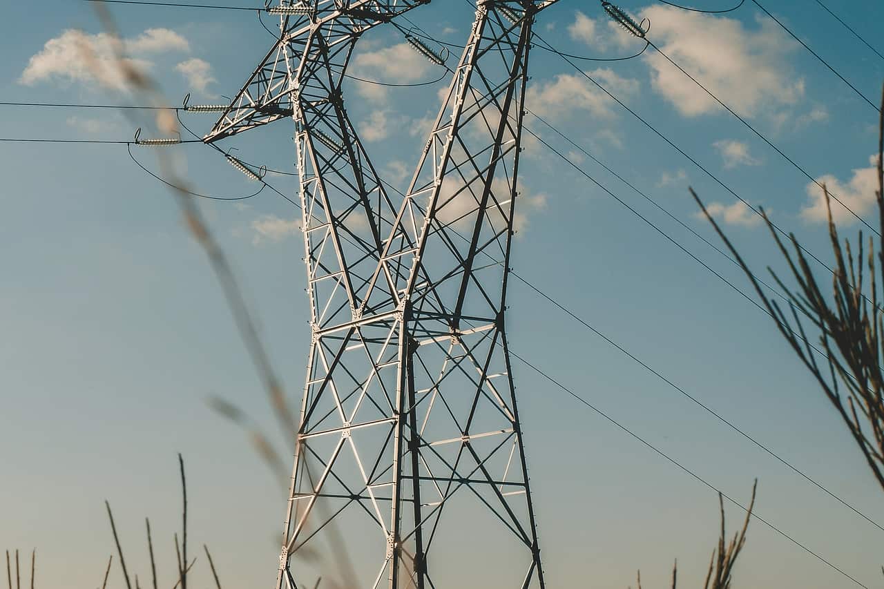 A steel transmission tower carrying power lines against a blue sky