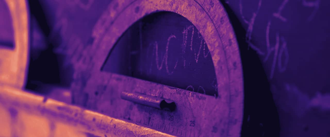 A wooden teaching protractor leaning against a chalkboard covered in numbers