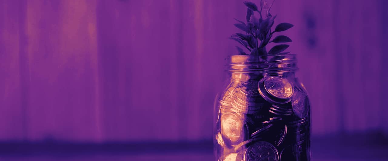 A glass jar of coins with a green plant growing from the top