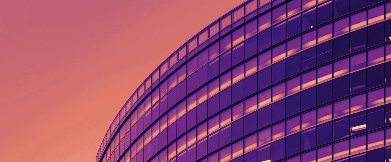 The curved blue glass facade of a mid-rise office building against the sky